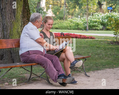 Il nonno e la sua nipote sta parlando e trascorrere del tempo insieme. Essi sono qui seduti sulla panchina del parco. Concetto intergenerazionale. Foto Stock