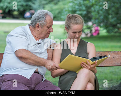 Il nonno e la sua nipote sta parlando e trascorrere del tempo insieme. Essi sono qui seduti sulla panchina del parco. Concetto intergenerazionale. Foto Stock