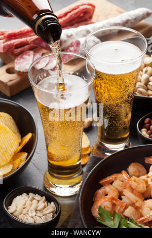 Progetto di birra e spuntini su sfondo di pietra. Dadi, patatine fritte, salsicce e gamberetti Foto Stock