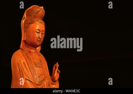 La religione buddista e la meditazione. Di Kannon o Guanyin, la Dea della Misericordia, statuetta in legno su sfondo nero (con copia spazio) Foto Stock