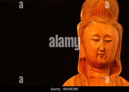 La religione buddista e la meditazione. Di Kannon o Guanyin, la Dea della Misericordia, statuetta in legno su sfondo nero (con copia spazio) Foto Stock