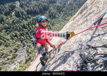 Una giovane donna è tutto sorrisi mentre jumaring su una corda fissa titolo in alto Foto Stock