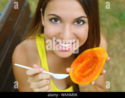 Ragazza mangiare sano papaia nel parco guardando la fotocamera. Donna di mangiare frutta tropicale all'aperto. Foto Stock