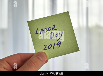 Una mano che tiene la Giornata del Lavoro scrivendo scritto su un foglietto adesivo Foto Stock