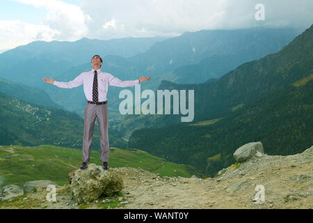 Un uomo d'affari spensierato in piedi sulla roccia con il braccio allungato Foto Stock