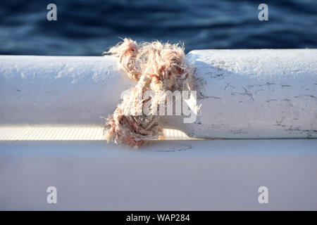 Fune spezzata legato con un nodo attorno a parte del vecchio pala in legno sulla barca bianca con mare blu superficie in background e spazio di copia Foto Stock