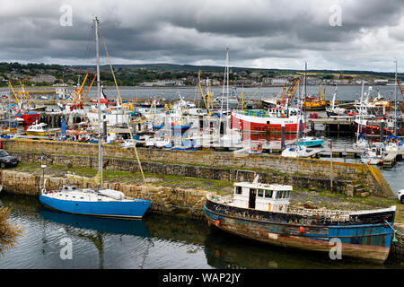 Vista di varie barche ormeggiate a pilastri di pietra di Newlyn Harbour con vista di Penzance attraverso Mounts Bay Cornwall Inghilterra Foto Stock