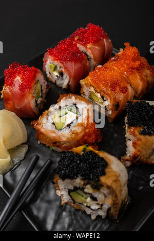 Rotolo di sushi di Philadelphia con salmone, anguilla affumicata, avocado, crema di formaggio su sfondo nero. Menu Sushi. Il cibo giapponese. Foto Stock
