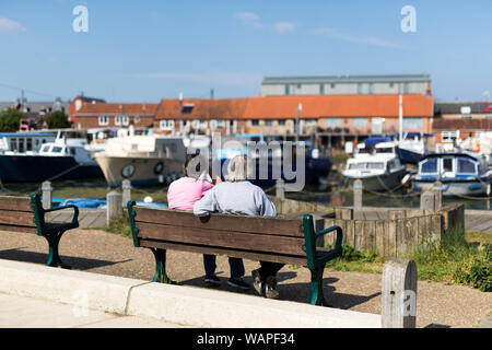 Una coppia di mezza età seduta su una panchina ammirando la schiera di diverse barche ormeggiate nel fiume Foto Stock