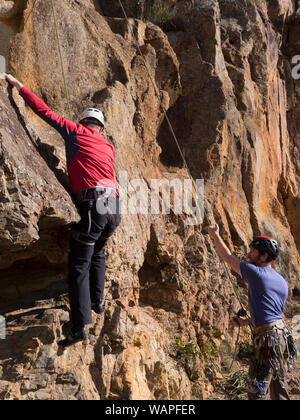 Tecnico istruttore di arrampicata, belaying un principiante alpinista e mostra paura, nervoso scalatore dove mettere le mani e i piedi sulla roccia in Australia. Foto Stock