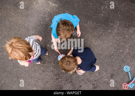 Guardando verso il basso su tre ragazzi giocare fuori con bolle Foto Stock