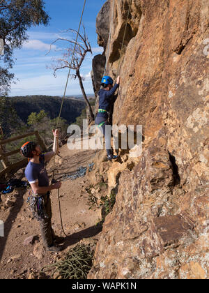 Tecnico istruttore di arrampicata, belaying un principiante alpinista e mostra paura, nervoso scalatore dove mettere le mani e i piedi sulla roccia in Australia. Foto Stock