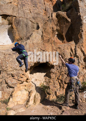 Tecnico istruttore di arrampicata, belaying un principiante alpinista e mostra paura, nervoso scalatore dove mettere le mani e i piedi sulla roccia in Australia. Foto Stock