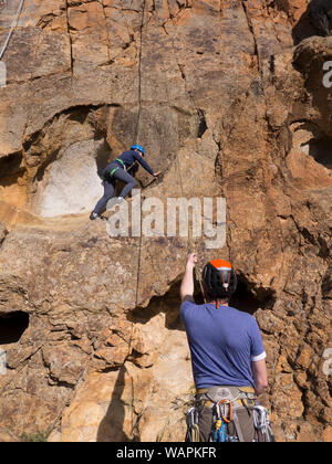 Tecnico istruttore di arrampicata, belaying un principiante alpinista e mostra paura, nervoso scalatore dove mettere le mani e i piedi sulla roccia in Australia. Foto Stock