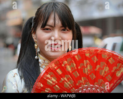 Giovane donna tailandese con lunghi pigtail posesg con un tradizionale hand-held ventola durante il Nuovo Anno Cinese. Foto Stock