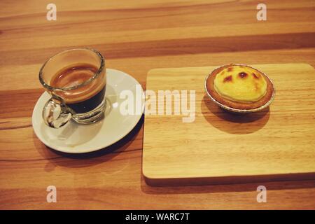 Torta di formaggio sul vassoio in legno e caffè espresso in vetro trasparente sul tavolo marrone Foto Stock