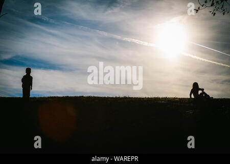 Silhouette ombre di due bambini su una collina con un cielo blu dietro di loro durante la riproduzione Foto Stock