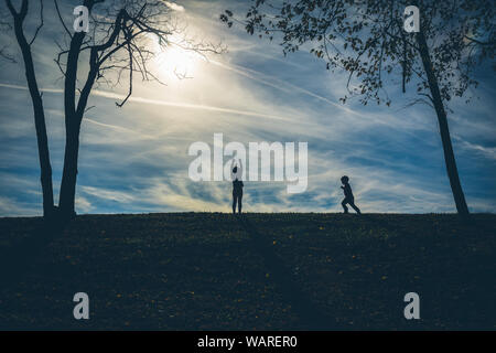 Silhouette ombre di due bambini su una collina con un cielo blu dietro di loro durante la riproduzione Foto Stock