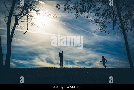 Silhouette ombre di due bambini su una collina con un cielo blu dietro di loro durante la riproduzione Foto Stock