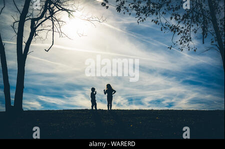 Silhouette ombre di due bambini su una collina con un cielo blu dietro di loro durante la riproduzione Foto Stock