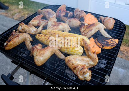 Estate barbecue per la cottura su un fuoco caldo con ali di pollo, bacchette e mais Foto Stock