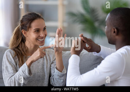 Sorridente etnia miste giovane parlando con il segno del dito lingua a mano Foto Stock