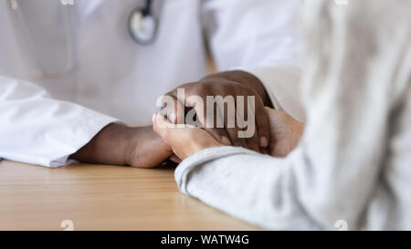 Grato paziente femmina tenendo le mani dell'Africano nero medico maschio Foto Stock