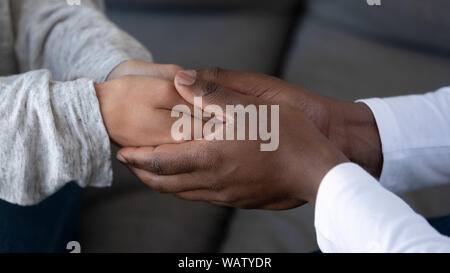 Chiusura del marito africano tenendo la mano della moglie bianca Foto Stock