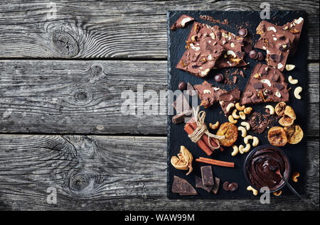 Cioccolato artigianale bar con fichi secchi e anacardi riempimento su un nero ardesia vassoio con ingredienti, vista orizzontale dal di sopra, flatlay, spazio vuoto Foto Stock