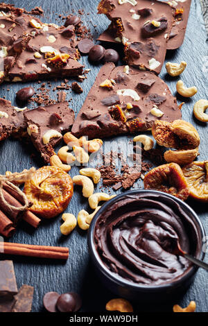 Deliziosi dolci della barra di cioccolato con fichi secchi e anacardi il riempimento su pezzi in un nero ardesia vassoio con ingredienti, vista verticale dal di sopra, close-up Foto Stock