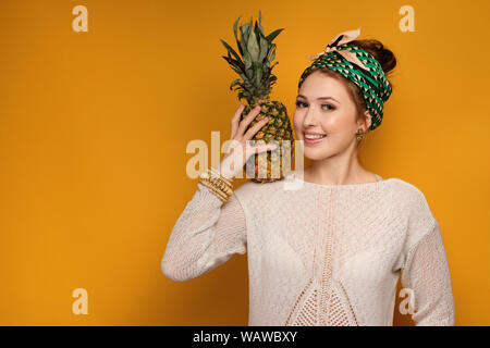 Ragazza in un maglione leggero ed annodato un velo è in piedi sorridente su sfondo giallo con un ananas sulla spalla. Foto Stock