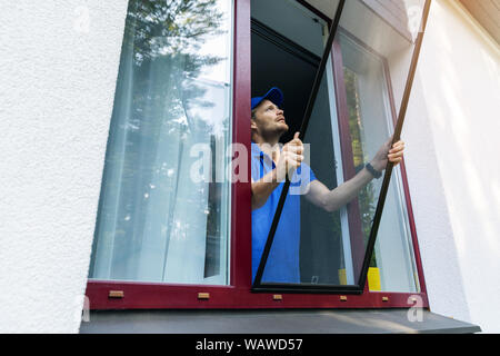 L'uomo installazione zanzariera wire mesh sulla finestra di casa Foto Stock