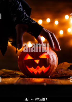 Immagine di sfondo di halloween con zucca e strega mano sul tavolo di legno contro il grunge bokeh sfondo luci Foto Stock