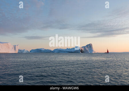 Little Red barca a vela navigando tra iceberg galleggianti nella baia di Disko glacier durante il sole di mezzanotte stagione di estate polare. Ilulissat. Unesco Foto Stock