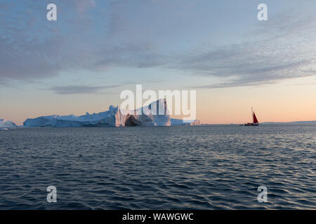 Little Red barca a vela navigando tra iceberg galleggianti nella baia di Disko glacier durante il sole di mezzanotte stagione di estate polare. Ilulissat. Unesco Foto Stock