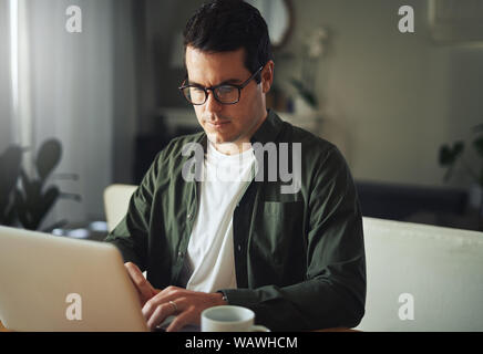 Uomo al lavoro seriamente sul portatile a casa Foto Stock