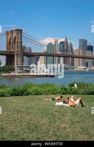 Estate di Brooklyn, vista degli uomini a prendere il sole nel parco stradale e principale di Brooklyn, con il ponte di Brooklyn e la parte inferiore dello skyline di Manhattan in distanza, NYC, STATI UNITI D'AMERICA