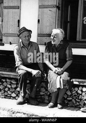 Vecchia coppia felice sulla banca della casa di fronte la fattoria, calzolaio Gaetano Anker con la sua donna Resi, intorno al 1960, Oberaudorf, Alta Baviera Foto Stock