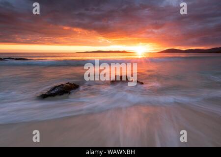 Rocce lavato mediante onde su una spiaggia di sabbia, drammatico tramonto con cielo nuvoloso sull'Oceano Atlantico, Isle of Harris, Scotland, Regno Unito Foto Stock