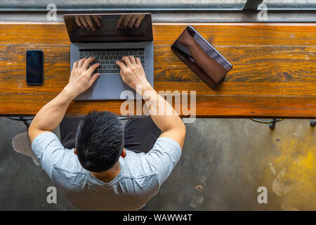 Asian freelancer digitando computer portatile accanto al tablet e smart phone Foto Stock