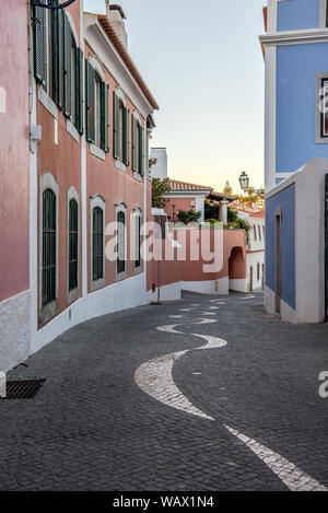 Avvolgimento acciottolato stretto vicolo in pavimentazione portoghese calçada modello di stile che conduce lontano tra tradizionale imbiancato e colorate case di pietra Foto Stock