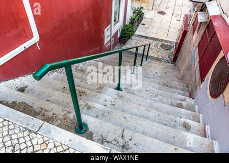 La scala in tradizionali pietre per pavimentazione con ringhiera verde che conducono alla pavimentazione in pietra alley tra colorate pareti di edifici in Cascais Portogallo Foto Stock