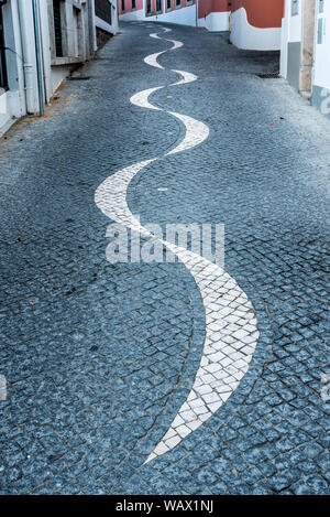 Avvolgimento acciottolato stretto vicolo in pavimentazione portoghese calçada modello di stile che conduce lontano tra tradizionale imbiancato e colorate case di pietra Foto Stock