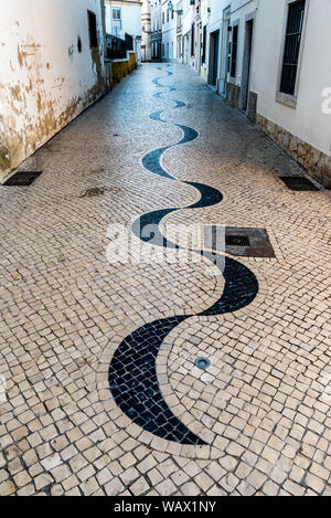 Avvolgimento acciottolato stretto vicolo in pavimentazione portoghese calçada modello di stile che conduce lontano tra tradizionale imbiancato e colorate case di pietra Foto Stock