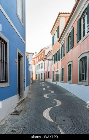 Avvolgimento acciottolato stretto vicolo in pavimentazione portoghese calçada modello di stile che conduce lontano tra tradizionale imbiancato e colorate case di pietra Foto Stock