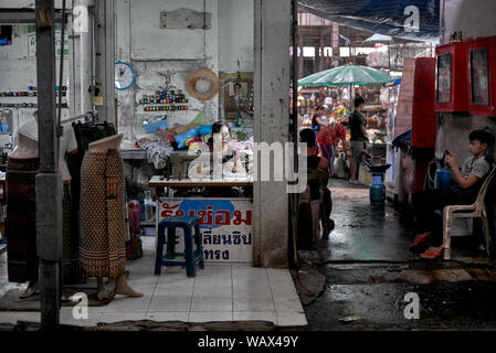 Donna che lavorano mentre ragazzo gioca con il suo smartphone. Thailandia indietro scene di strada Foto Stock