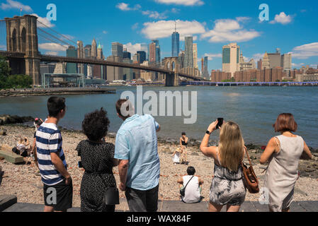 Spiaggia ghiaiosa Brooklyn estate, vista posteriore di persone in piedi sulla spiaggia di ciottoli e guardando attraverso l'East River a Manhattan, New York City, Stati Uniti d'America. Foto Stock