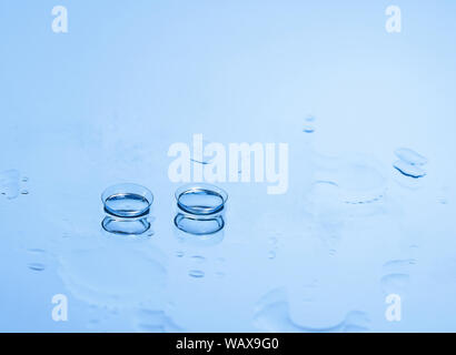 Le lenti a contatto per gli occhi sul vetro tra le gocce di acqua in blu. Apparecchiature ottiche, buona visione, all'ottico optometrista. Foto Stock