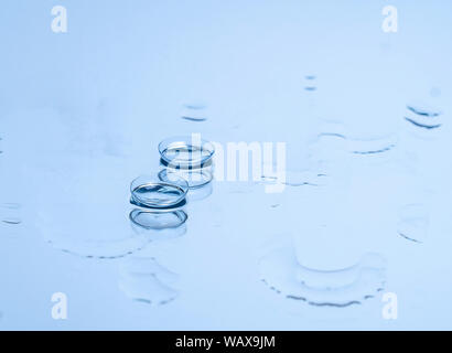 Le lenti a contatto per gli occhi sul vetro tra le gocce di acqua in blu. Apparecchiature ottiche, buona visione, all'ottico optometrista. Foto Stock