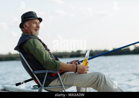 Uomo sorridente mentre godendo di pesca notturna e bere birra Foto Stock